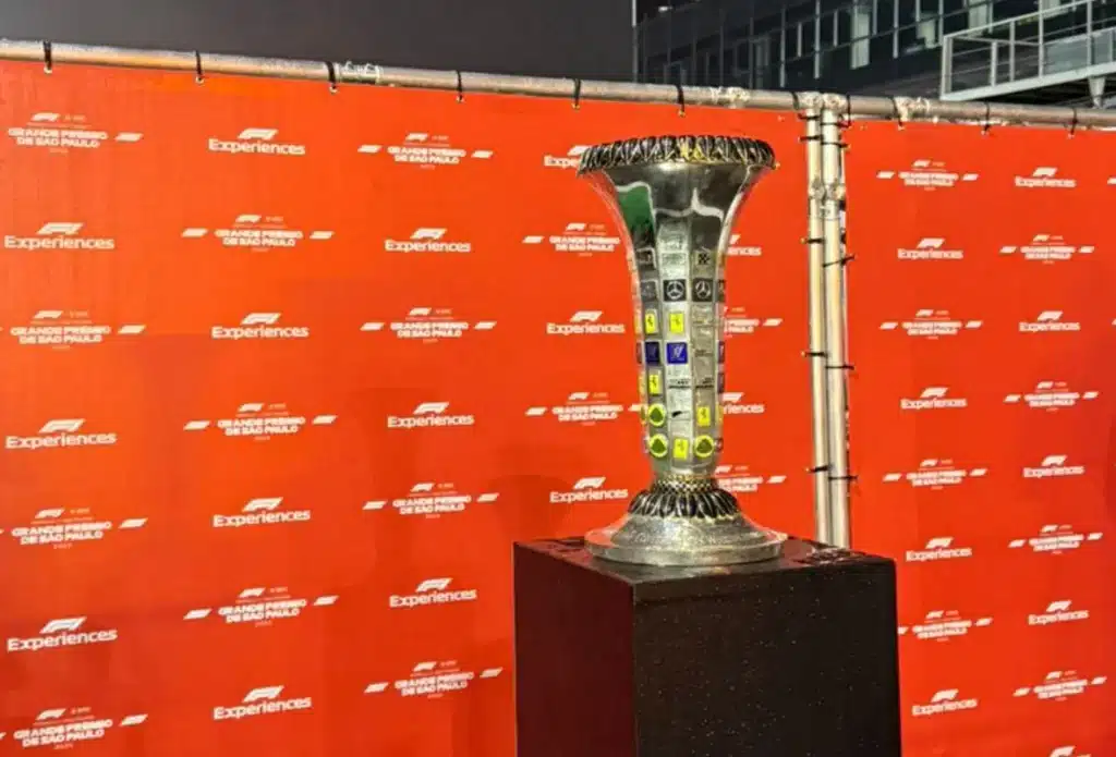 F1 luxury vacation package  Championship trophy on a dark pedestal in front of an orange F1 Experiences backdrop at Interlagos.