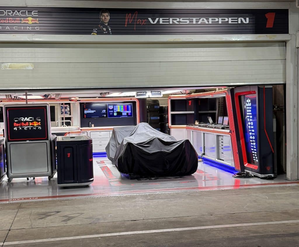 Formula 1 sponsorship Oracle Red Bull Racing branding above and inside Max Verstappen’s garage at Interlagos, with a covered car and wet pit lane.