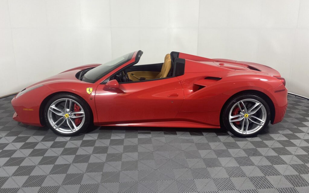A red Ferrari convertible in side profile, with its roof down and both wheels visible.