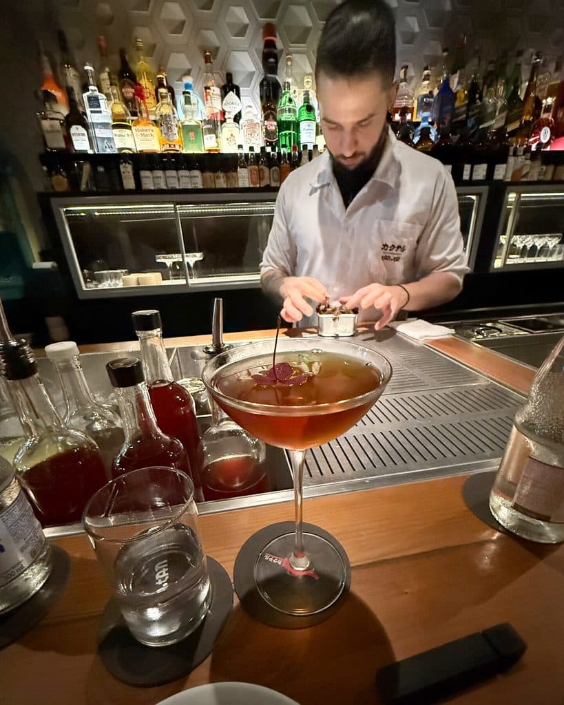 A bartender works behind the Tan Tan bar, with an amber cocktail in the foreground and bottles behind him.