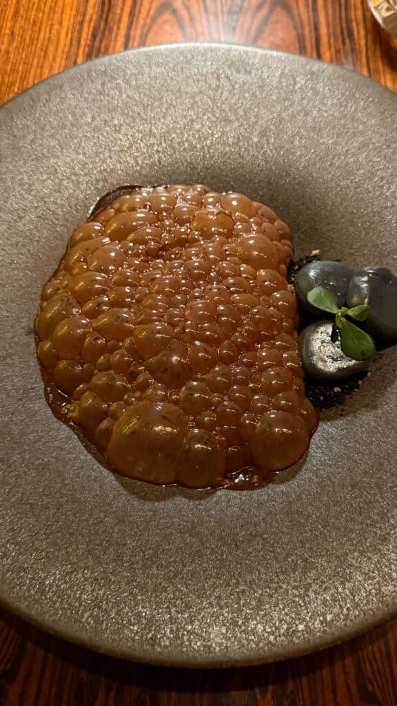 A golden textured course with a small garnish on a grey ceramic plate at D.O.M.