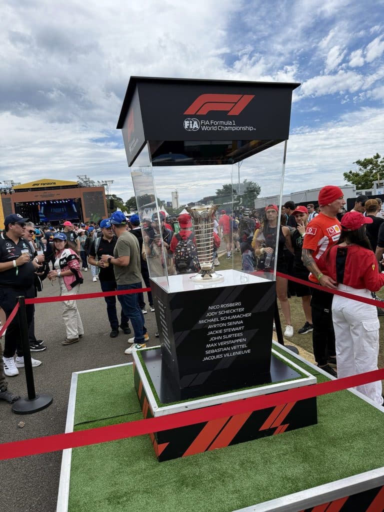 History of Autodromo Jose Carlos Pace Formula 1 championship trophy displayed in a glass case among fans at Interlagos.