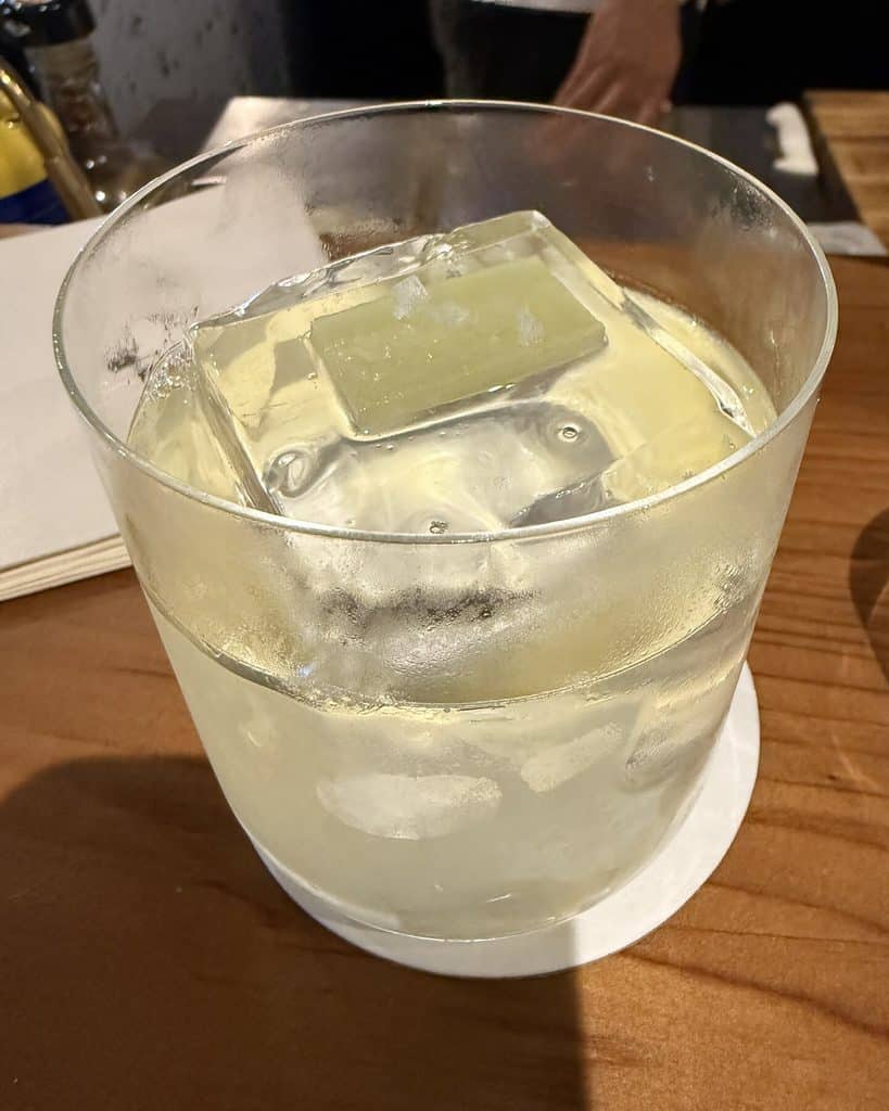 A pale cocktail with a large rectangular ice block in a rounded glass on the wooden bar at Tan Tan.