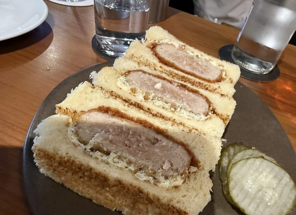 Three pieces of breaded katsu sandwich on soft white bread, served with a pickle slice at Tan Tan.