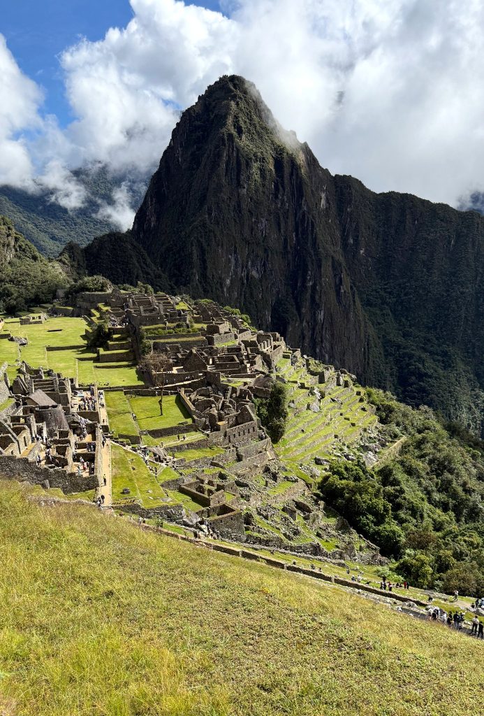 Stone terraces and ruins at Machu Picchu beneath a steep mountain and scattered clouds.