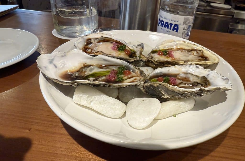 Four dressed oysters on the half shell arranged on a white plate at Tan Tan.