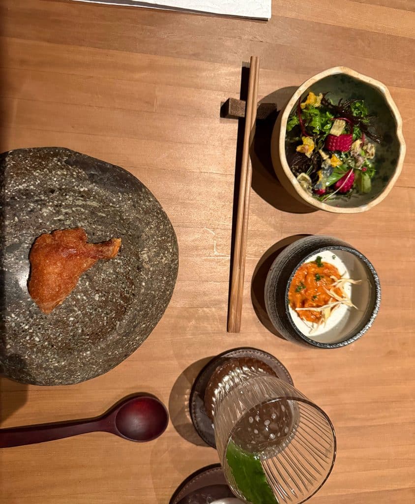 An overhead view of several dishes, chopsticks and a drink on a wooden counter at Maido.