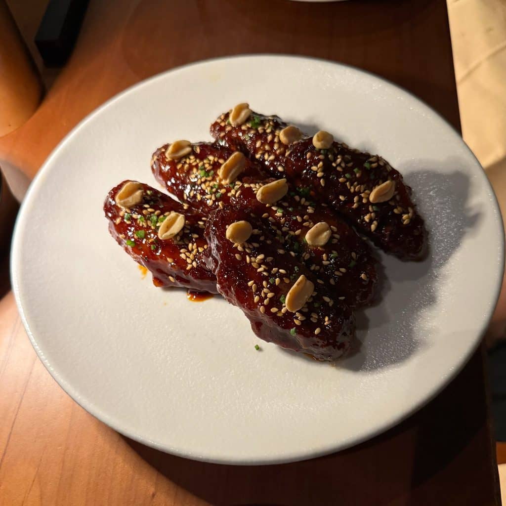 Glossy chicken wings topped with sesame seeds and peanuts on a white plate at Tan Tan.