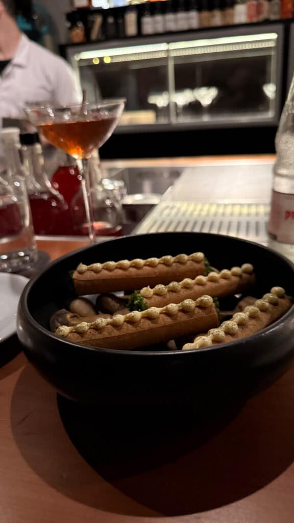 Food served in a black bowl beside a stemmed cocktail at the Tan Tan bar.