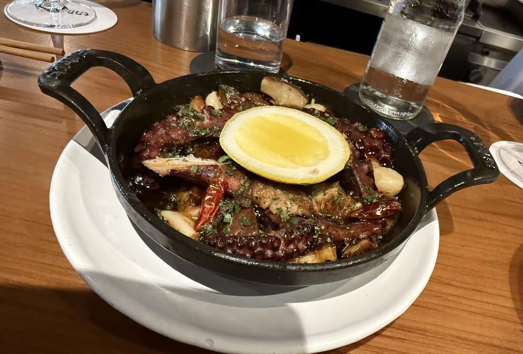 Octopus and mushrooms topped with a lemon slice in a black handled pan at Tan Tan.