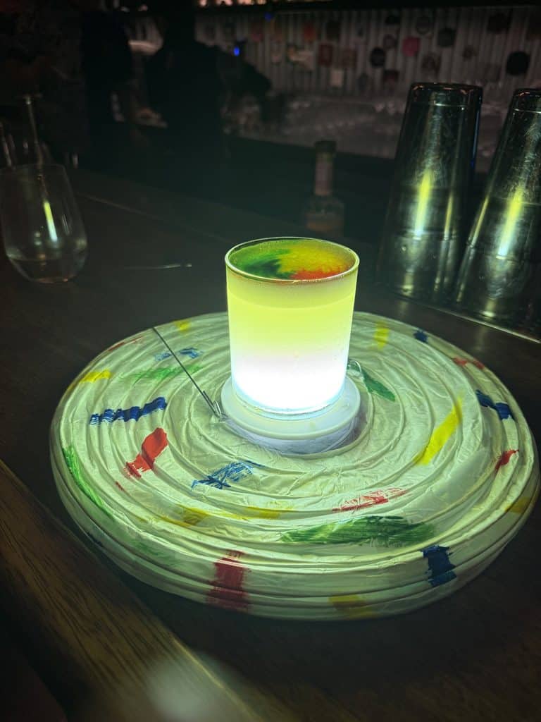 A luminous green cocktail on a broad, multicolored circular serving plate at Carnaval in Lima.