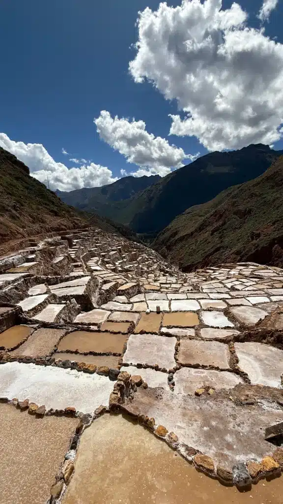 Saying Yes White salt terraces stepping down a mountainside beneath a cloudy sky in Peru