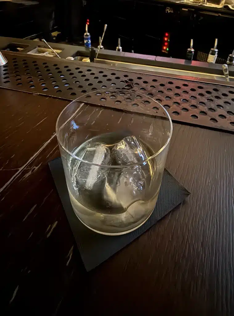 F1 luxury vacation package  A short cocktail glass with a large ice cube on a dark wooden bar at Sir Victor in Barcelona.