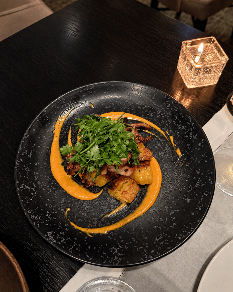 Dish with fresh herbs and orange sauce on a black plate beside a candle at Tangará Jean-Georges.
