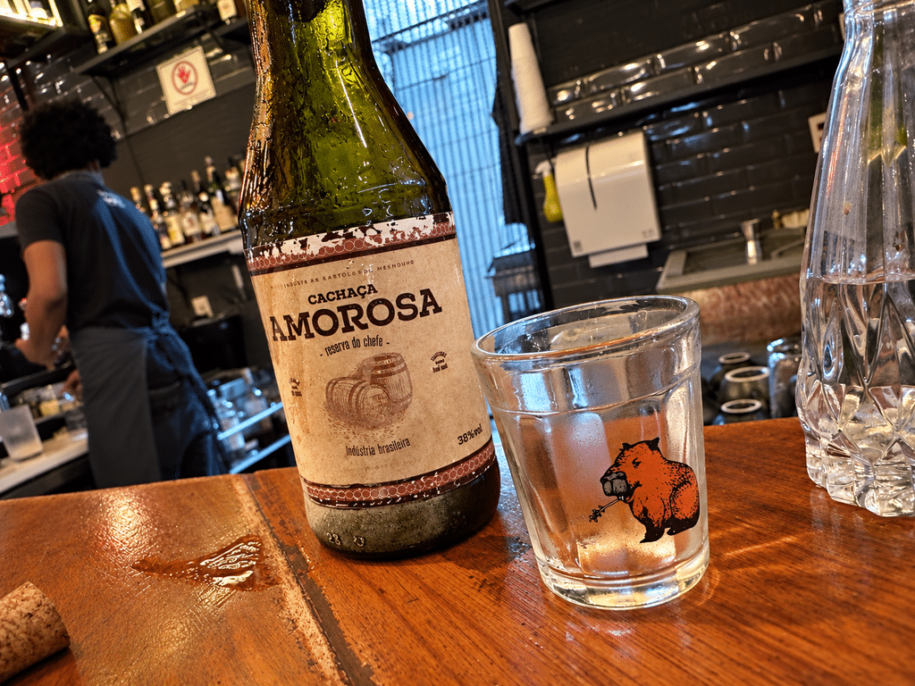 A Casa do Porco review: A bottle of Cachaça Amorosa Reserva do Chefe beside a small pig-illustrated glass at A Casa do Porco.