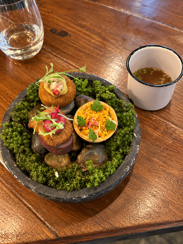 A Casa do Porco review: three colorful tasting-menu bites presented on moss and stones beside a small cup.