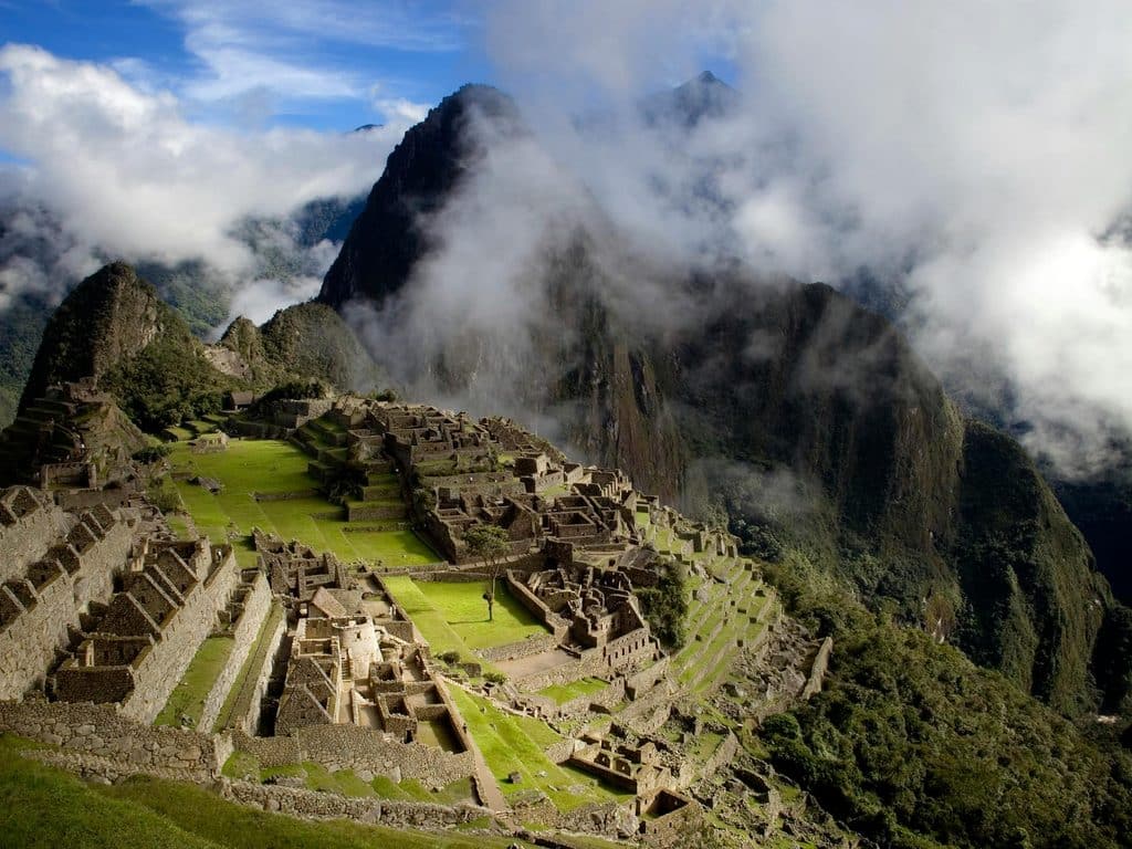 Peru Travel Plans Stone terraces and Inca ruins at Machu Picchu beneath steep, cloud-covered mountains in Peru.