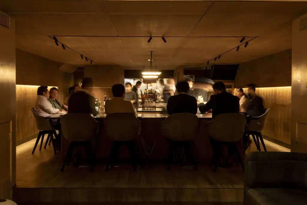 Exclusive Restaurants Intimate counter dining room at Atomix in New York City, with guests seated around the open kitchen during service.