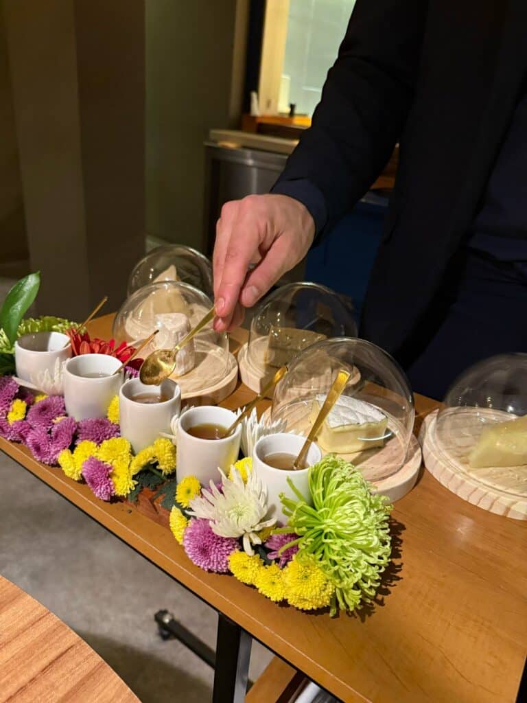 Server presenting cheeses under glass domes and small cups of honey at Evvai.
