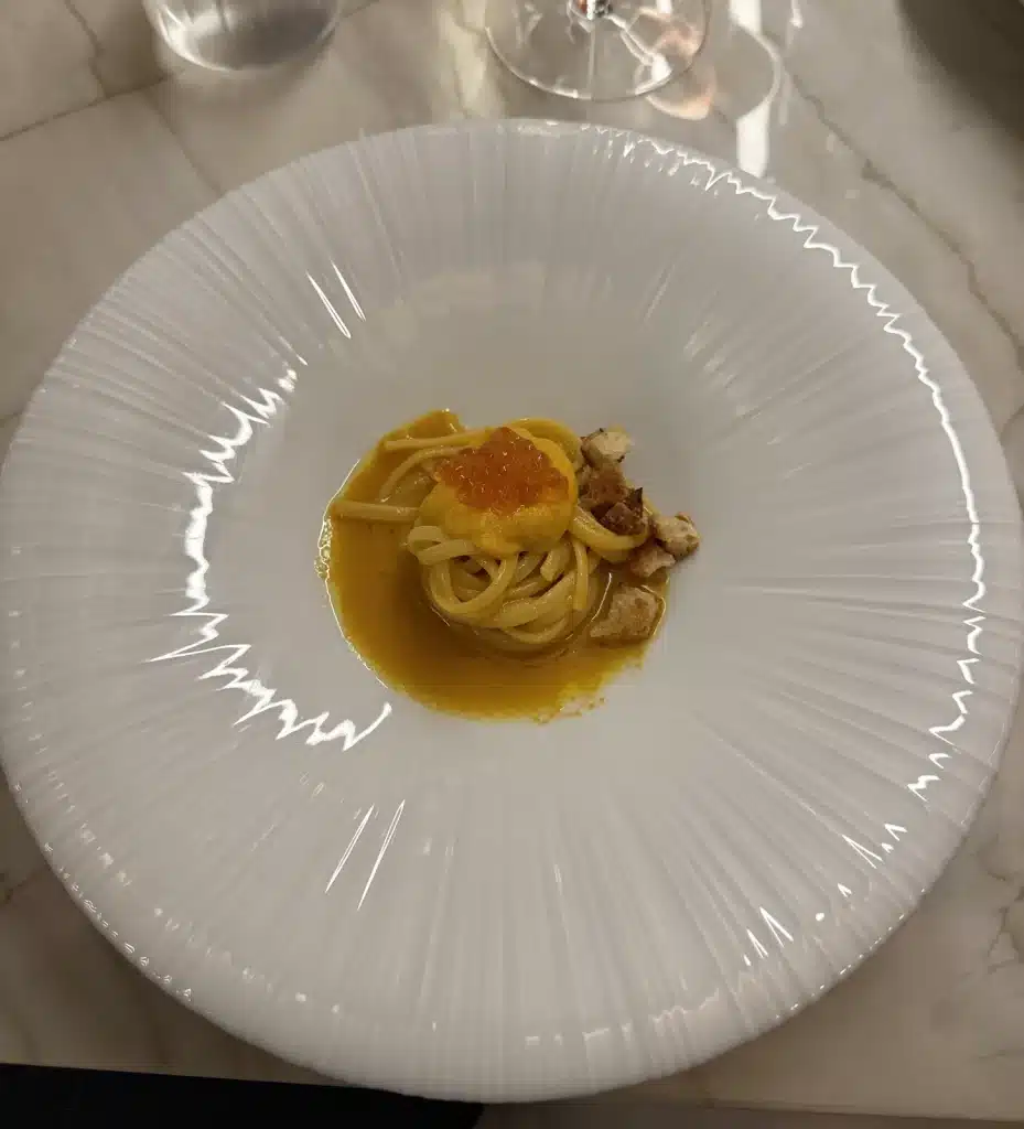 Nelita São Paulo Overhead view of a nest of pasta in golden sauce, topped with orange pearls, on a white plate at Nelita.