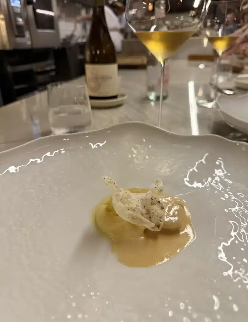 Nelita São Paulo A plated course in pale sauce with a crisp garnish, with white wine and a bottle behind it at Nelita.