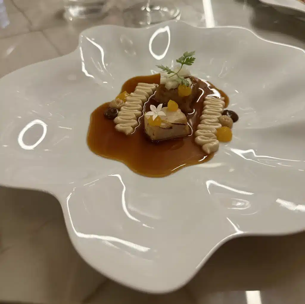 Nelita São Paulo A plated course in brown sauce with piped accompaniments, small flowers and herbs on a wavy white plate at Nelita.
