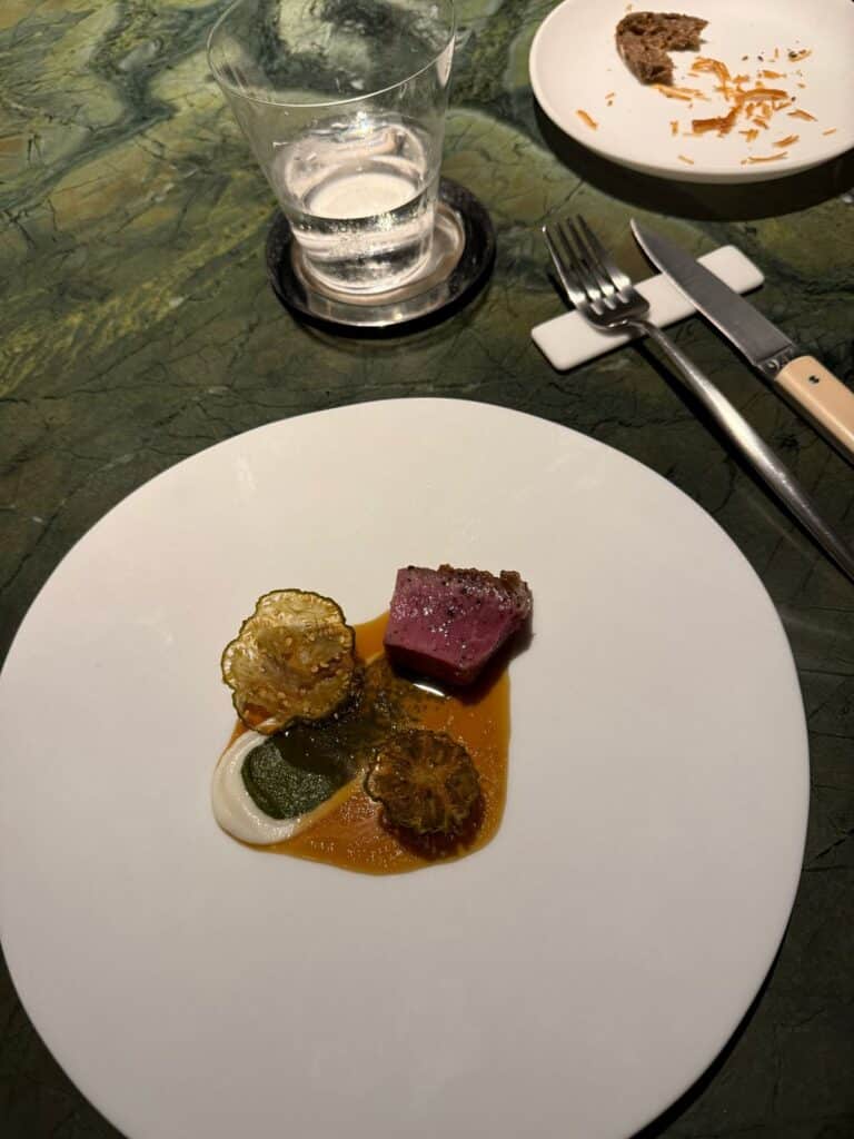 Pink-centered lamb with vegetables and contrasting sauces on a white plate at Tuju.