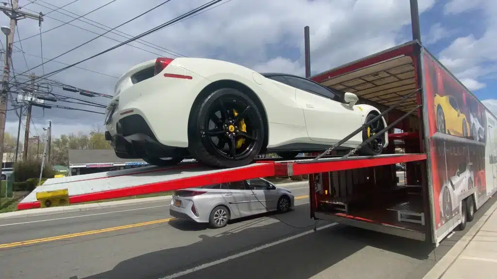 FROM SUPERCARS TO SUITCASES A white Ferrari on the loading platform of a vehicle transporter beside a road.