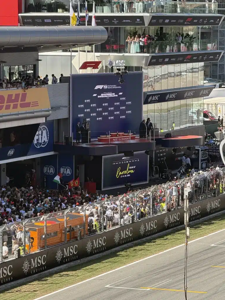 FROM SUPERCARS TO SUITCASES Spectators gather below the Barcelona circuit podium, viewed across the pit straight and safety fence.