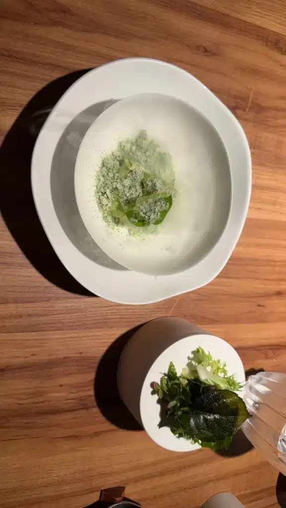 Green course in a white bowl with a separate small plate of greens at Evvai in São Paulo