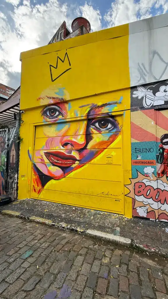 Travel Research A colorful face painted on a bright yellow wall beside the cobbled lane at Beco do Batman in São Paulo.