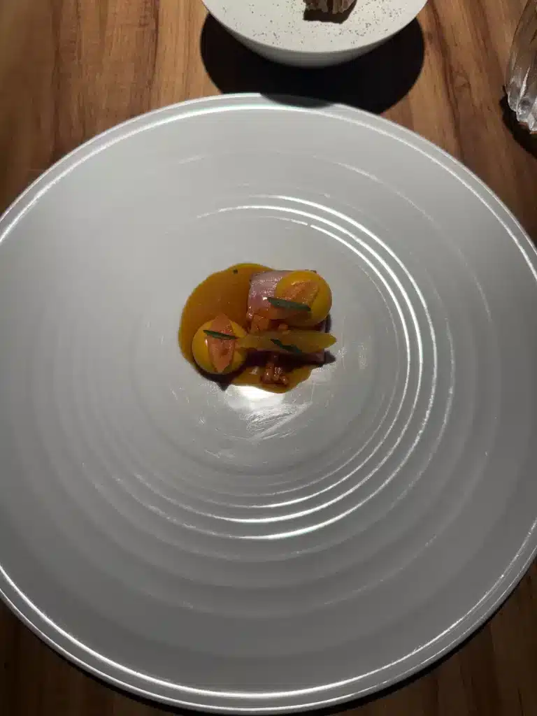 Small plated savory course with orange sauce in a wide white bowl at Evvai in São Paulo
