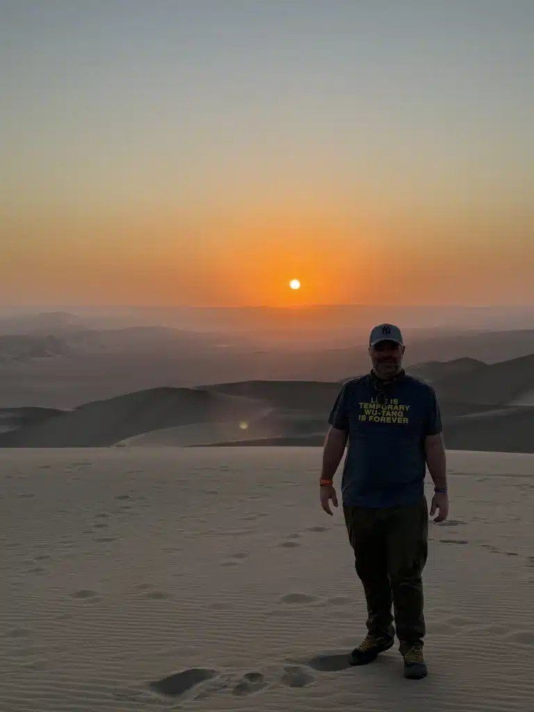 Richard Jarocki standing on sand dunes at sunset, with rolling desert ridges behind him.