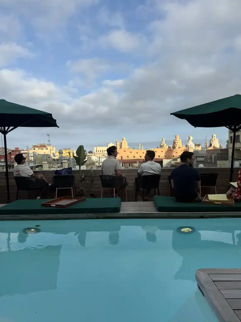 Travel Research The rooftop pool and terrace at Sir Victor in Barcelona, with seated guests and city buildings beyond.