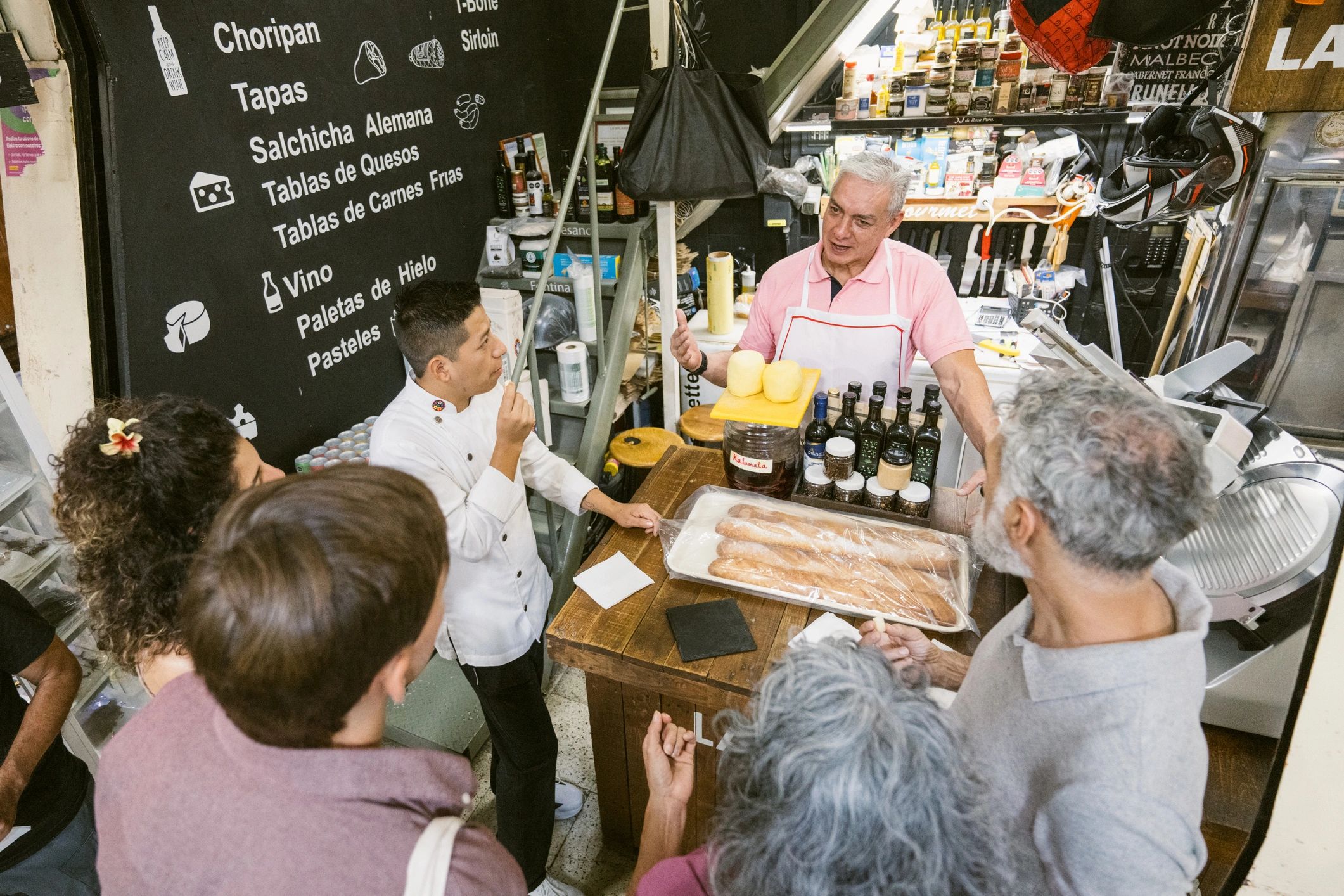 Delicatessen market stall owner talks to a group of tourists