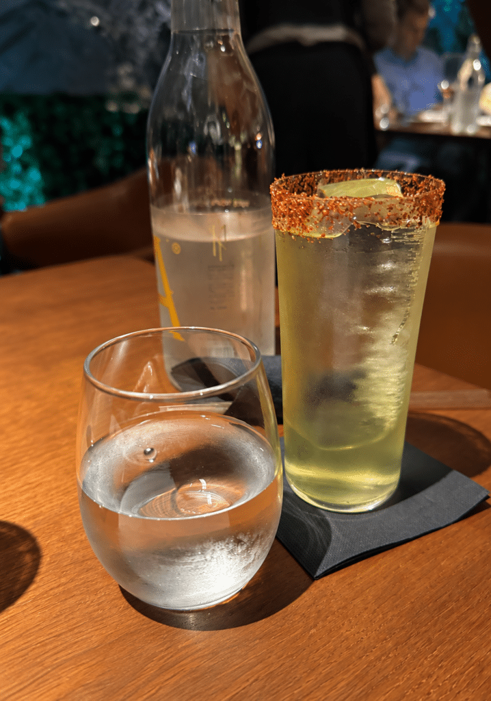 Formula 1 Tall iced cocktail with a seasoned rim beside a water glass on a wooden table at MR PORTER Barcelona.