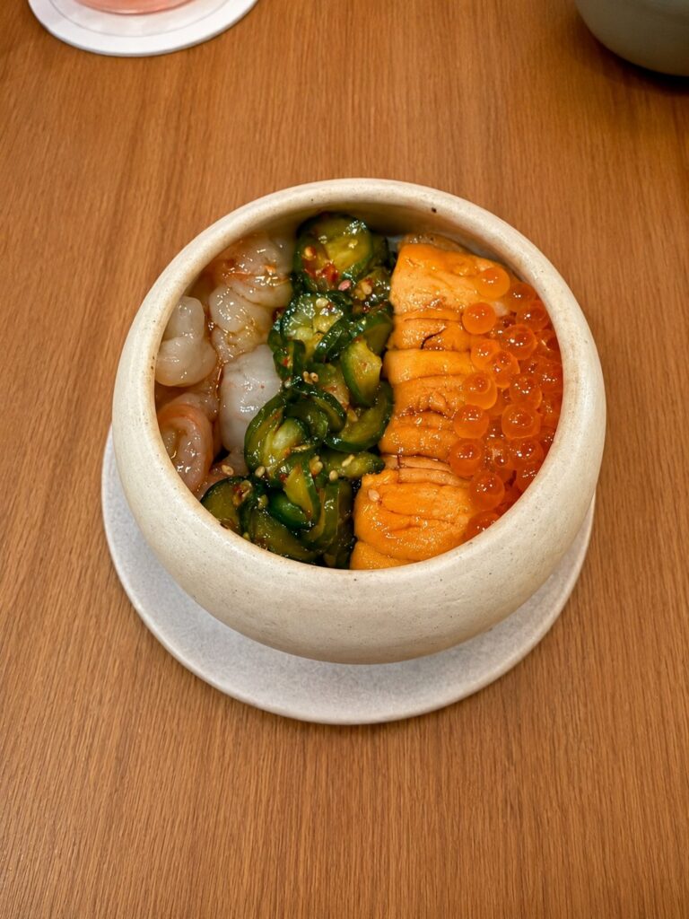The Oiji Bowl at Michelin-starred Oiji Mi in New York City is served in a handcrafted ceramic bowl and features Hokkaido sea urchin, sweet spotted prawn, salmon roe, Oiji sauce, and seasoned seaweed rice arranged in neat sections.