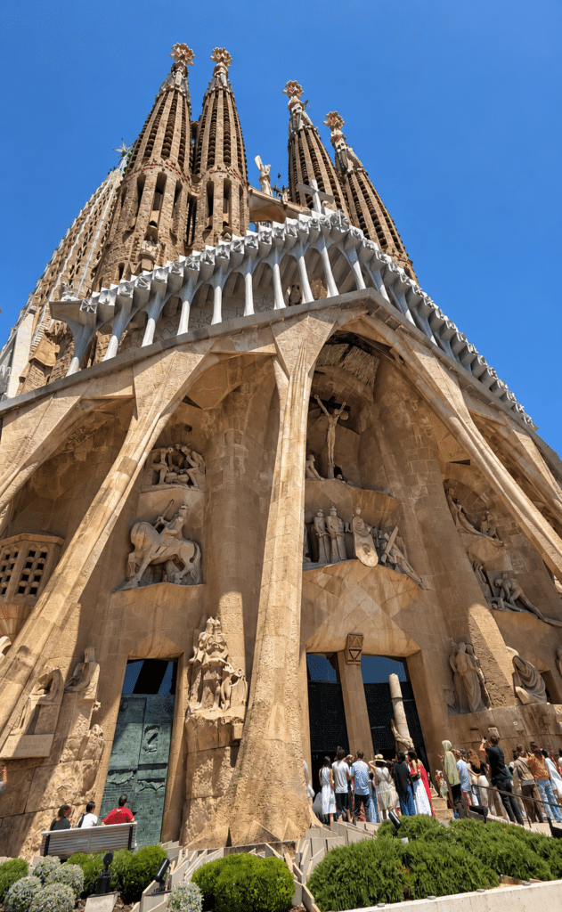 Formula 1 Sagrada Família’s stone facade and four spires rising above visitors beneath a blue sky.