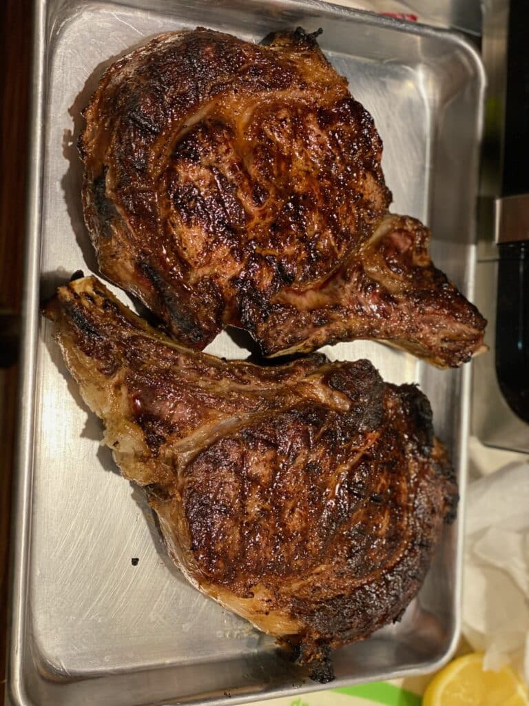 Two bone-in ribeye steaks resting after cooking with a deeply browned crust