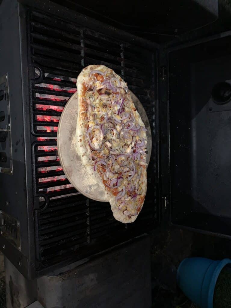 Homemade chicken and red onion pizza cooking on a stone inside an outdoor grill