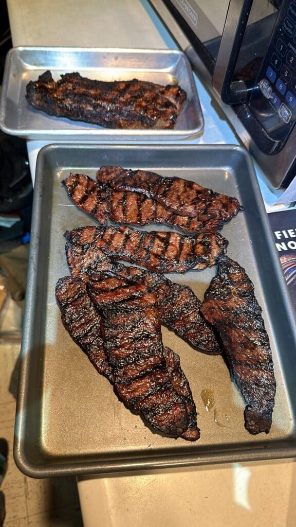 Grilled steaks with caramelized crusts resting on metal trays