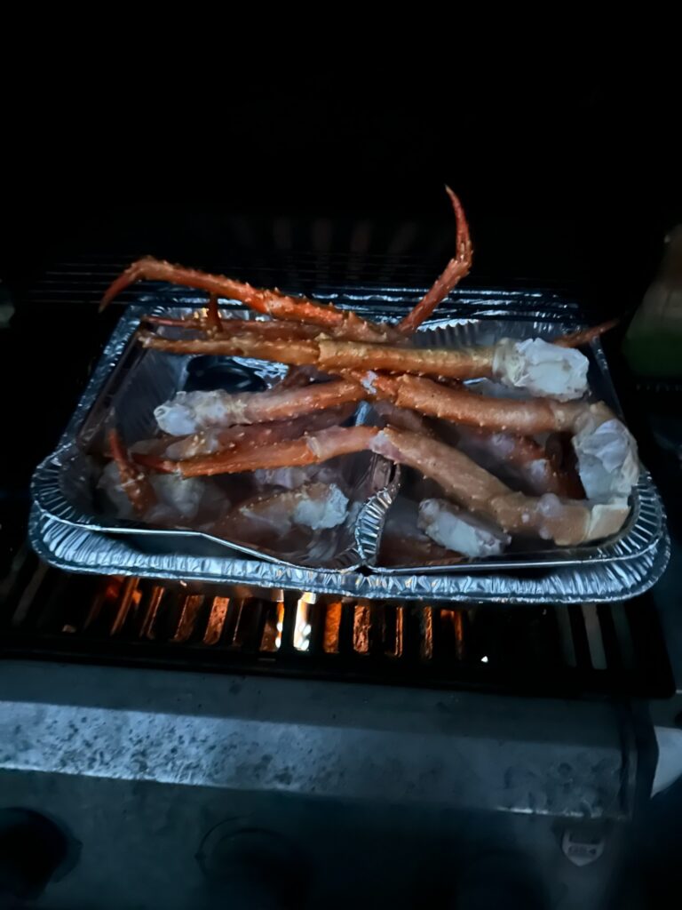 King crab legs warming in foil pans over an outdoor grill