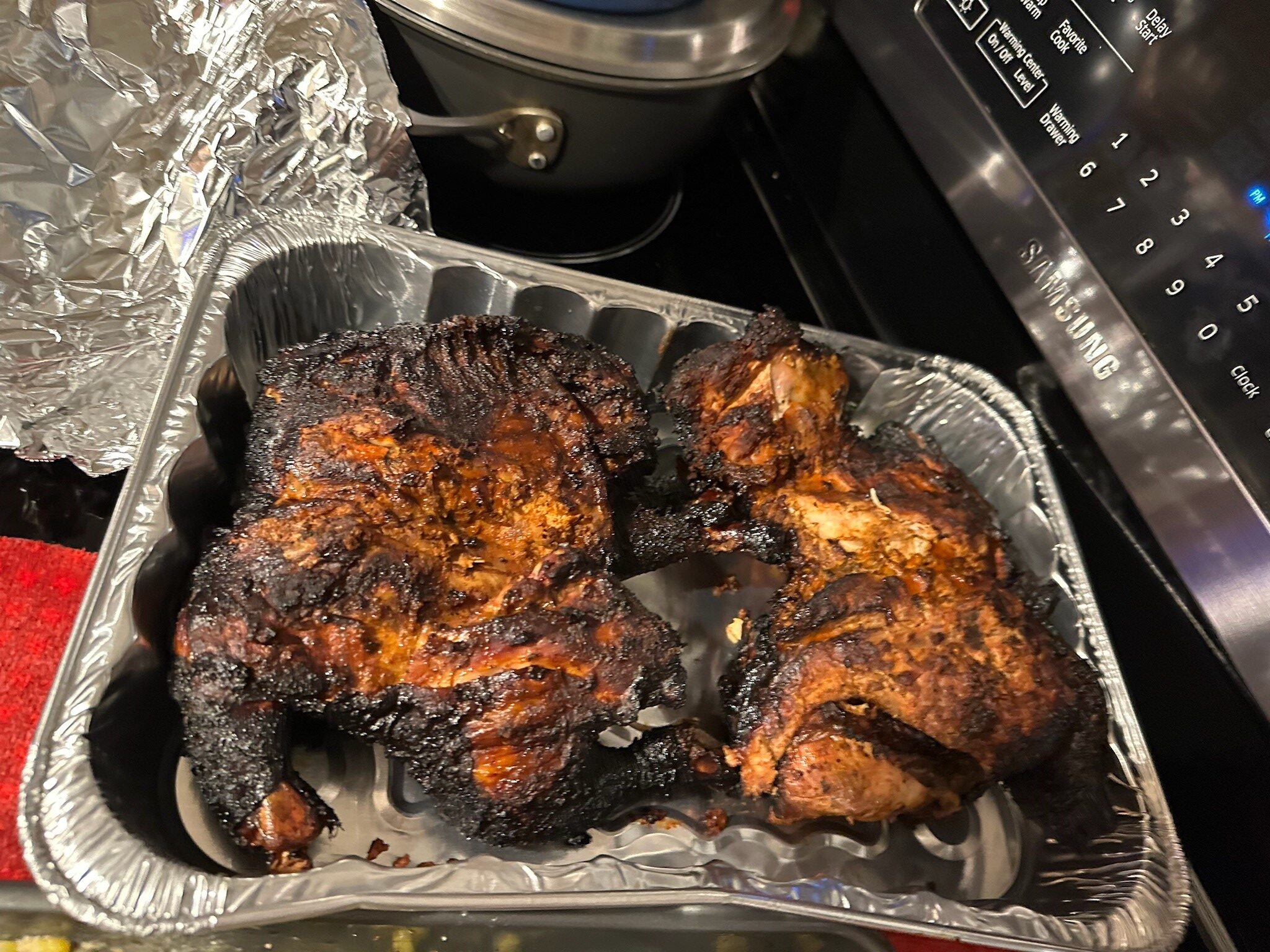Seasoned roasted chicken pieces with a deeply browned crust in a foil pan