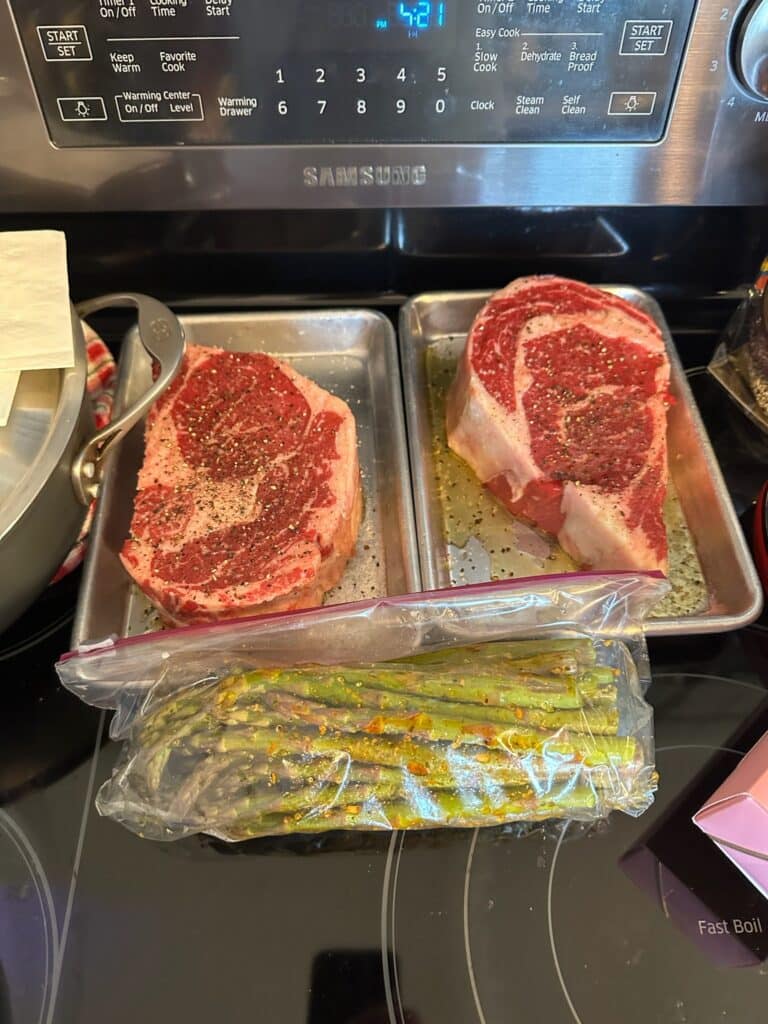 Two seasoned ribeye steaks with marinated asparagus ready for cooking