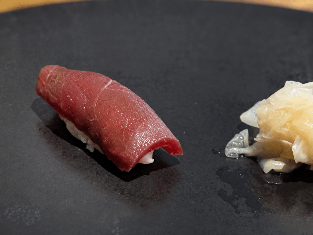 Lean, deep-red akami tuna nigiri with pickled ginger on a black plate at the Dassai Blue omakase.