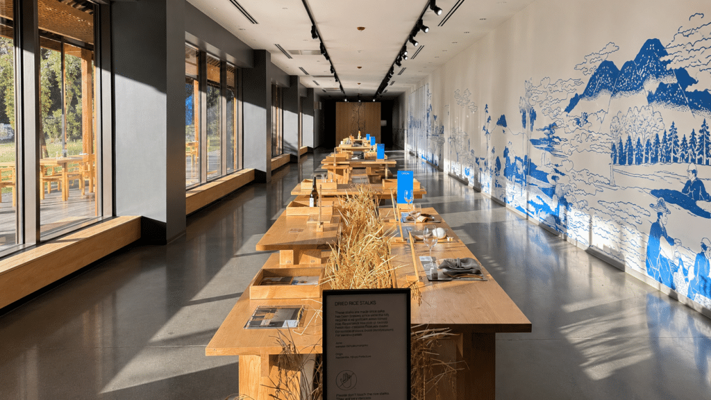 Sunlit main foyer and sake exhibition at Dassai Blue Brewery in Hyde Park, New York, with wooden displays and a blue-and-white mural.