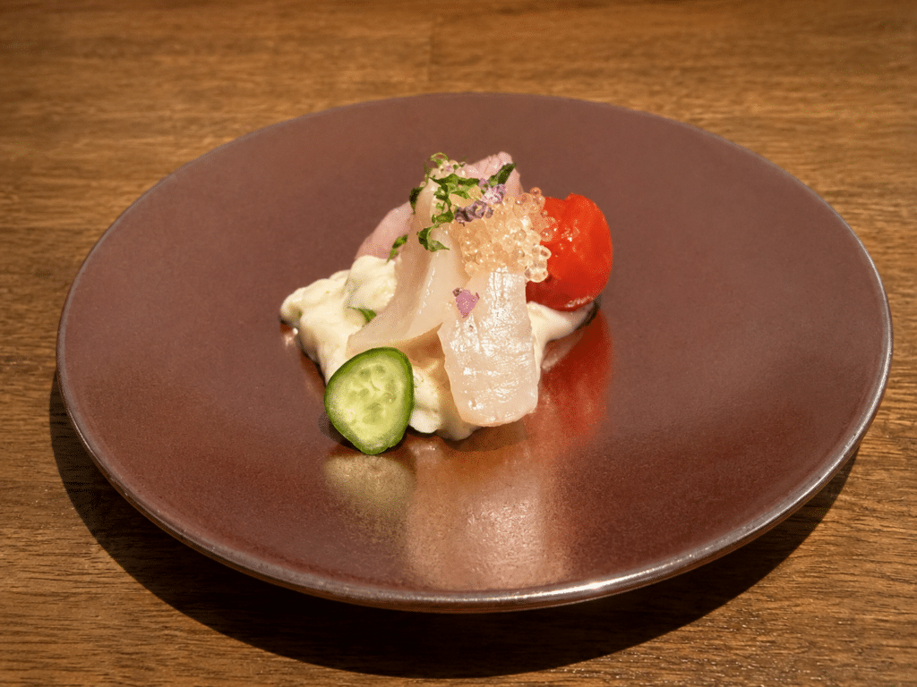 Medai snapper ceviche with sake lees, cucumber and tomato on a brown plate.