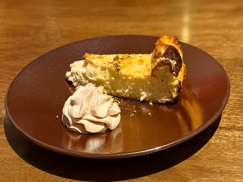 A slice of brûléed cheesecake with piped cream on a brown plate at the Dassai Blue omakase.