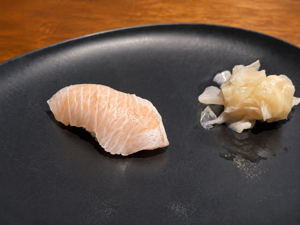 Pale pink, richly marbled toro nigiri with pickled ginger on a black plate at the Dassai Blue omakase.