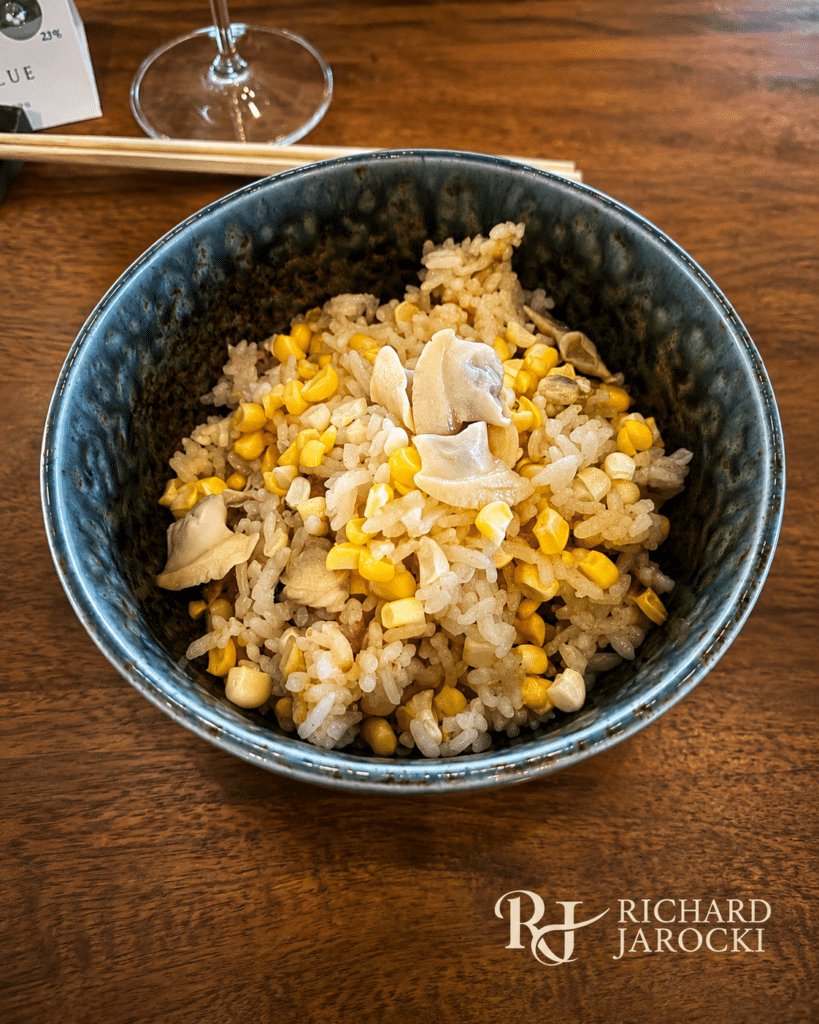 Locally grown rice with sweet corn and clams in a dark ceramic bowl.